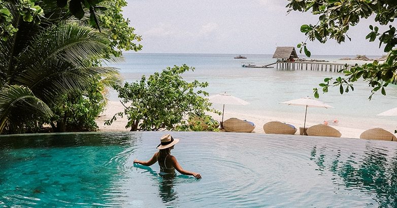 A woman in a stylish hat stands in a resort pool, representing influencer marketing in the hospitality industry.