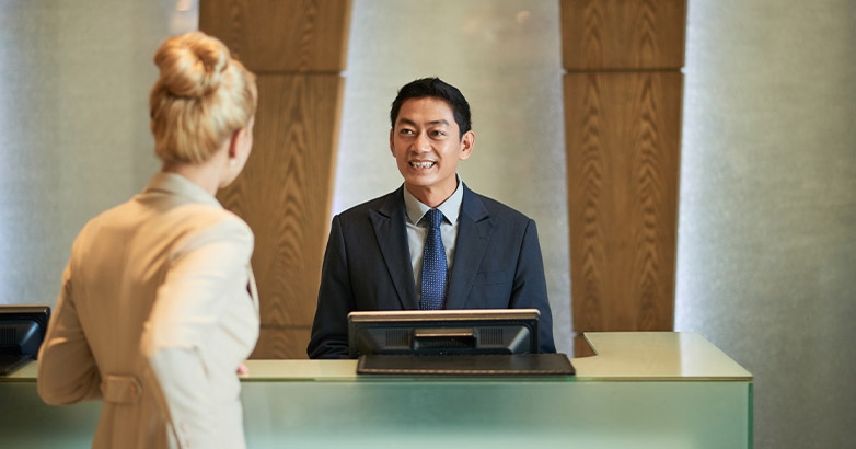 A man and woman engage with staff at a reception desk, highlighting marketing in the hospitality and tourism industry.