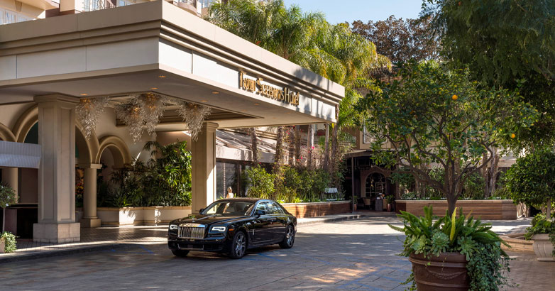 A luxury black car parked in front of the Four Seasons Hotel.
