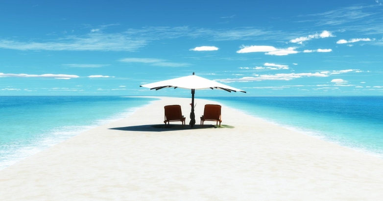 Two comfortable chairs are positioned under an umbrella on a sandy beach, ideal for relaxation at Musha Cay.
