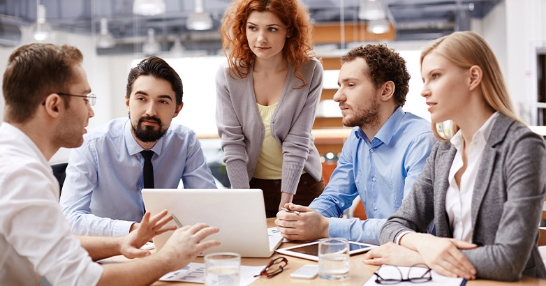 A team gathered around a table with a laptop, engaged in discussions about leveraging guest surveys for hotel reputation management.