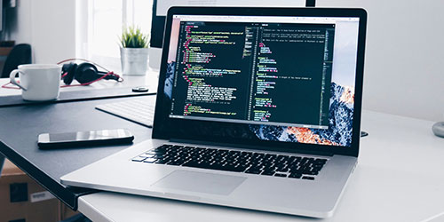 Developer coding on a laptop with HTML and CSS code visible on screen.