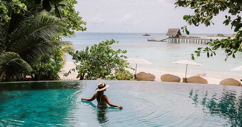 The tourist enjoys swimming in the large outdoor pool of the luxury hotel with an overlooking view of the sea.