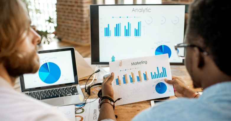Two people analyzing graphs on a computer screen related to hotel marketing channels and performance tracking.