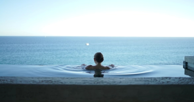 A woman enjoys a peaceful moment in a pool, overlooking the ocean, highlighting a luxurious hotel atmosphere.