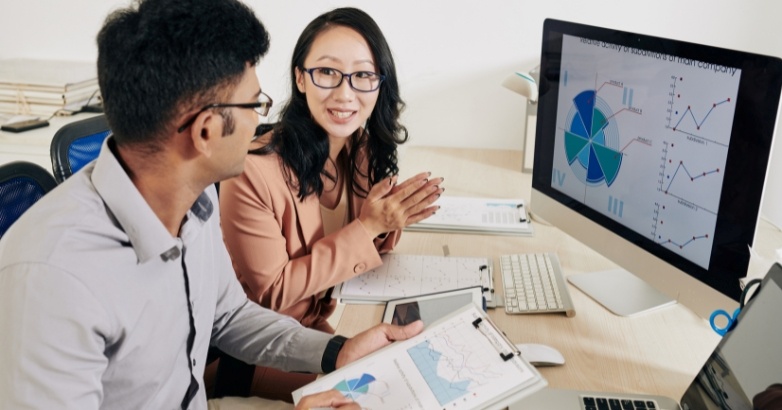 Two individuals reviewing a computer screen featuring graphs that illustrate video performance metrics for hotel marketing.