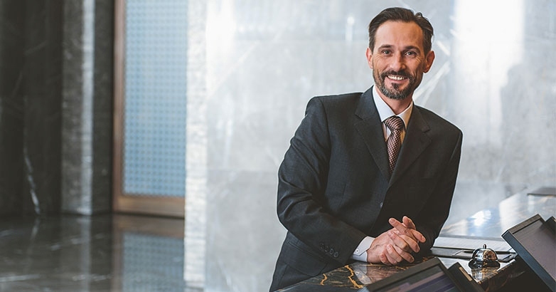 A man in a suit stands at the hotel front desk, representing a strategic partner in hotel advertising.
