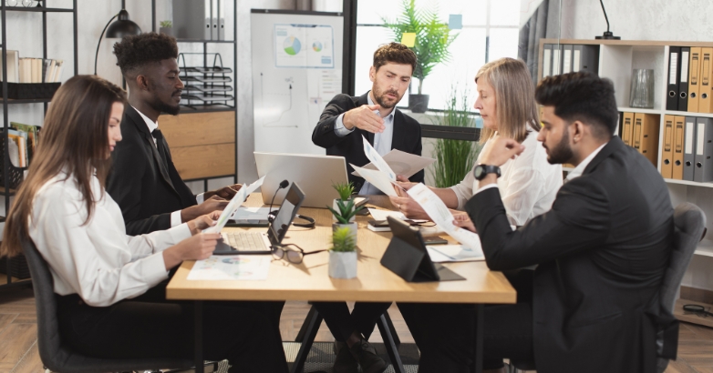A group of business professionals engaged in discussion around a table during a hotel marketing audit meeting.