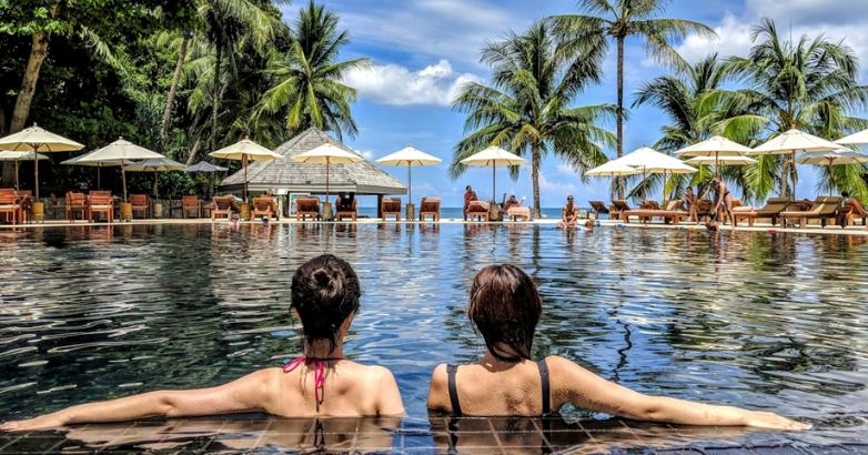 Two women relax in a resort pool, enjoying the sun and each other's company, embodying local experiences in hotel marketing.