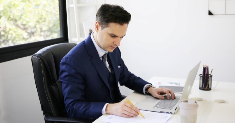 A suited man at a desk with a laptop, focused on a report about marketing and distribution assets for hotels.