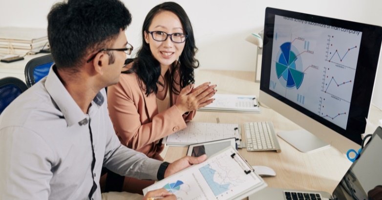 Two people discussing a hotel marketing audit while reviewing a computer screen displaying a SWOT or gap analysis.