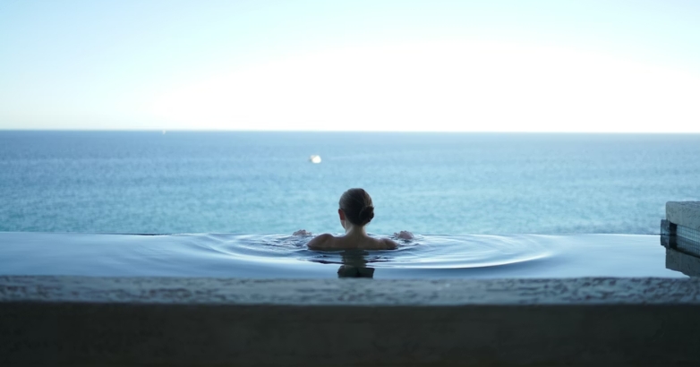 A woman enjoys a peaceful moment in a pool, overlooking the ocean, highlighting a luxurious hotel atmosphere.