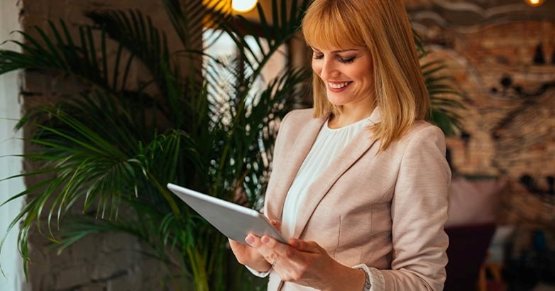A woman in a professional suit is holding a tablet, symbolizing innovative trends in hotel website design and voice search.