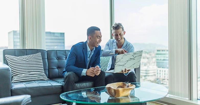 Two men seated on a couch, looking at a computer screen featuring travel advertising that impacts buying choices.