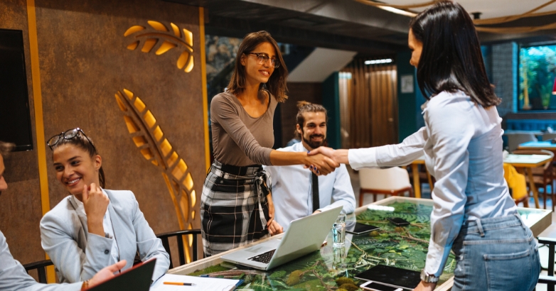 Business individuals engaging in a handshake at a conference table, deliberating on hotel marketing agency expertise.