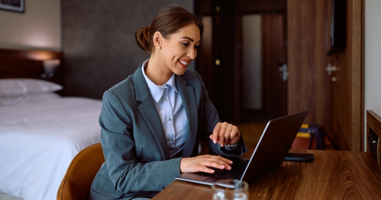 A woman dressed in a business suit is seated at a table with a laptop, contemplating hotel marketing agency choices.