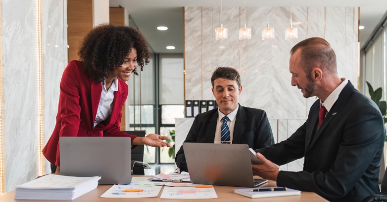 Three business people collaborating at a table with laptops, comparing proposals for hotel marketing agency strategies.