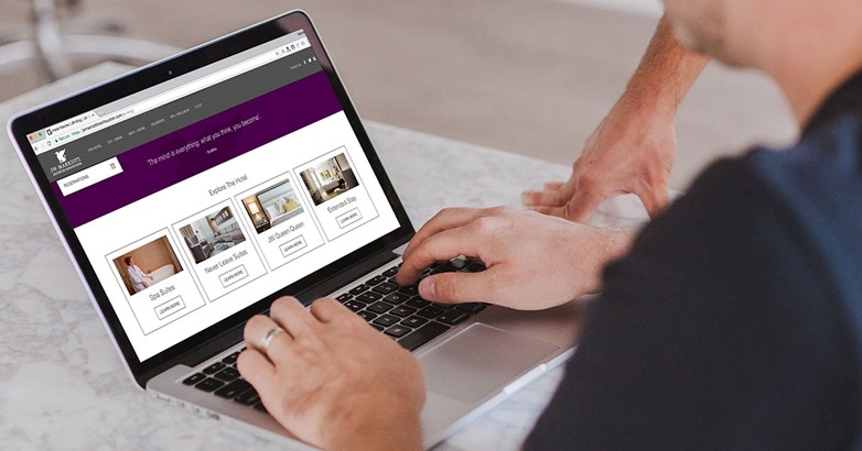 A man engaged with a laptop showing a purple website dedicated to hotel branding and visual identity creation.
