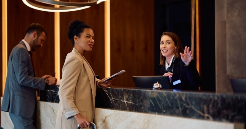 A woman in a tailored business suit stands at the front desk, illustrating effective guest engagement strategies for hotels.