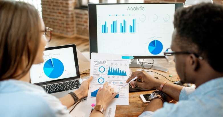 Two professionals examining graphs on a computer, discussing analytics related to digital marketing services for hotels.