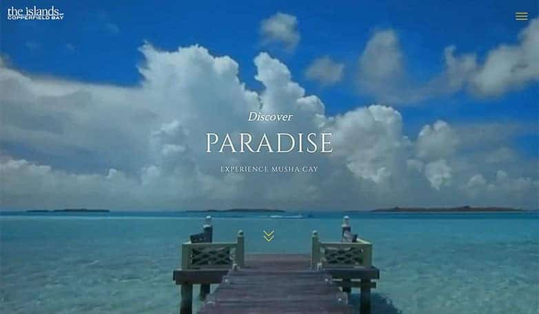 A scenic view of a wooden pier extending into turquoise waters under a blue sky with fluffy clouds, promoting Musha Cay.
