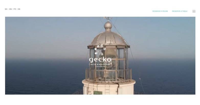 A lighthouse with a metallic dome, overlooking the ocean, featuring the logo for Gecko Hotel & Beach Bar.