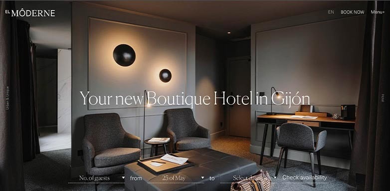 A stylish hotel room featuring modern decor, two armchairs, a coffee table, and a desk, with soft lighting and neutral tones.