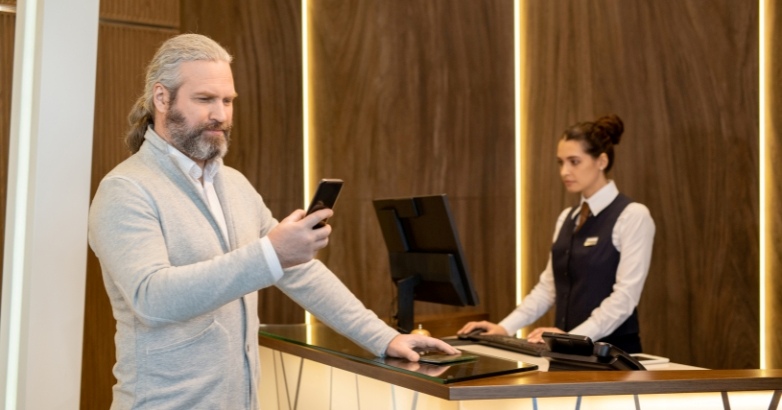 A man stands at the hotel front desk, with a woman behind him, illustrating mobile marketing tips for hotels.