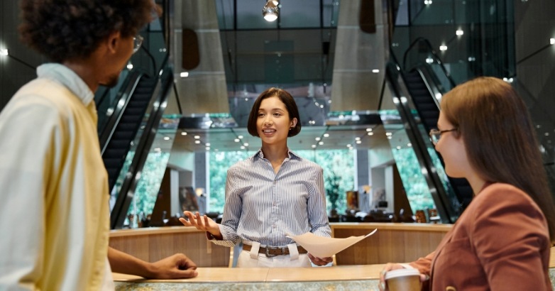 A woman stands at a hotel front desk, embodying authentic hospitality and meaningful guest experiences.