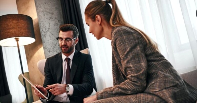 A man and woman dressed in business attire, sitting in a hotel room, focused on storytelling to improve guest experiences.