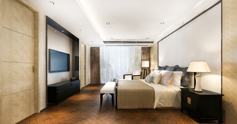 A modern hotel bedroom featuring a large bed and a television, showcasing smart room technology in the AI hotel industry.