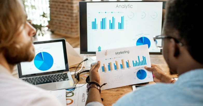 Two professionals examining graphs on a computer screen about the ROI of content marketing for hotels.