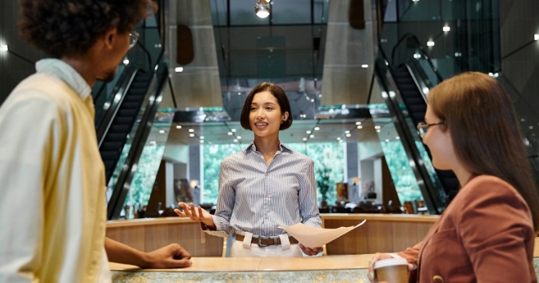 A woman stands at a hotel front desk, representing the blend of digital and on-site experiences in hotel marketing.
