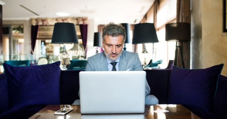 A suited man on a couch uses a laptop, focusing on the future of hotel website design and personalized guest experiences.